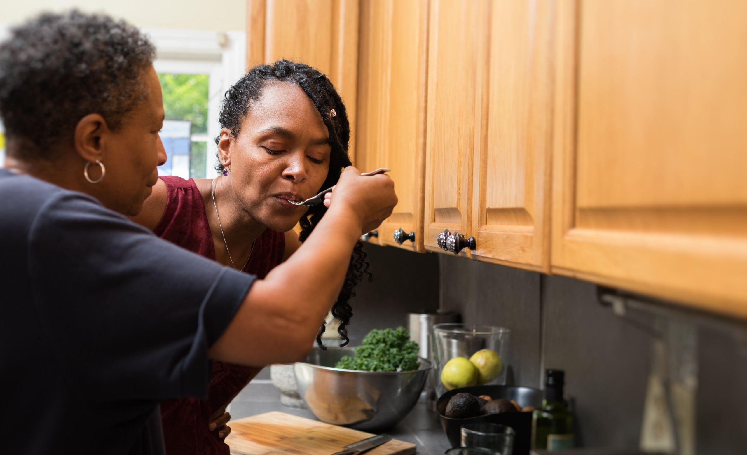 One woman feeding another woman food in a kitchen