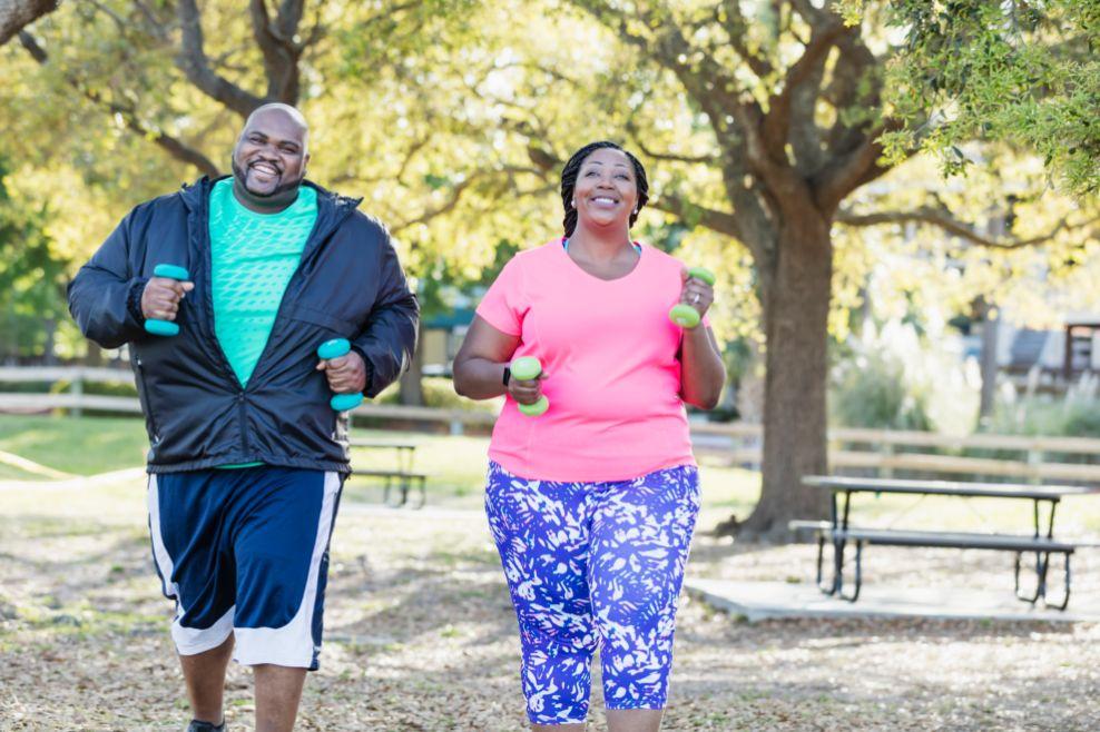 A man and woman running with weights in the park